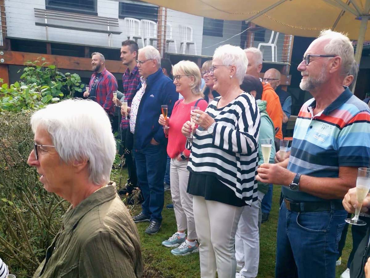 Mitglieder stehen mit Getränken in der Hand zusamen und hören Renate bei der Taufe des Motorbootes zu.