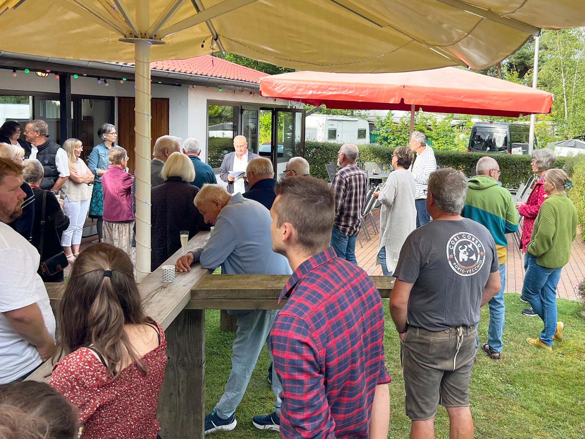 Mitglieder stehen zusammen und hören dem Vorsitzenden bei seiner Rede zu